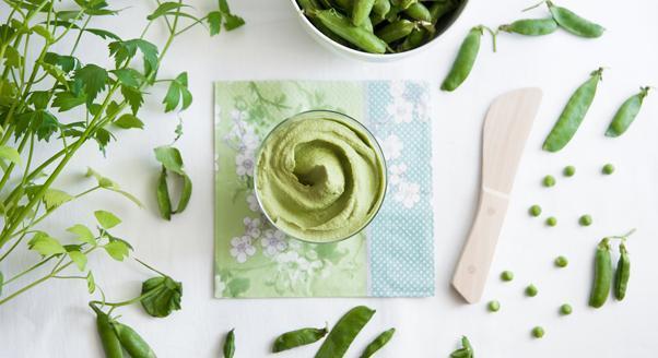Znudziło ci się tradycyjne pesto? Zaszalej ze składnikami i odkryj jego smak na nowo! – zdjęcie numer 1 Tekst o lokalnych składnikach do tworzenia pesto. Na zdjęciu: Miska z zielonym sosem obok groszku i drewniana łyżka - HelloZdrowie