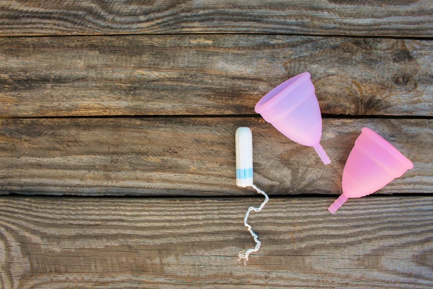 Tampon i dwa kubeczki menstruacyjne, na drewnianym tle