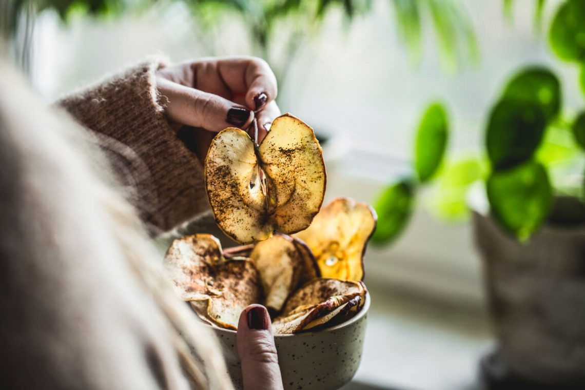 Tekst o zdrowej alternatywie dla chipsów: suszone jabłka. Na zdjęciu: Osoba trzymająca miseczkę chipsów - HelloZdrowie