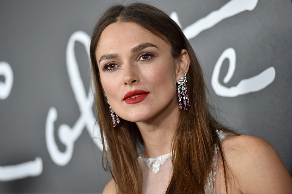 Aktorka, Keira Knightley pozuje do zdjęć. Zdjęcie do klatki piersiowej, kobieta ma ciemne, rozpuszczone włosy, pomalowane na czerwono usta i duże kolczyki.
