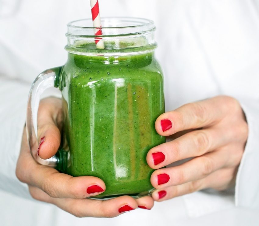 Tekst o zdrowych przekąskach do pracy zamiast kanapek. Na zdjęciu: Osoba trzymająca zielony smoothie w słoiku szklanym - HelloZdrowie