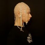 Zuzanna Bartoszek pozuje bokiem na czarny tle w czarnej bluzie z koralami na głowie