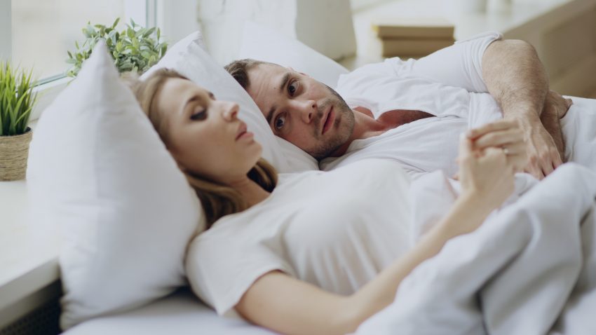 para leży w łóżku z białą pościelą i rozmawia