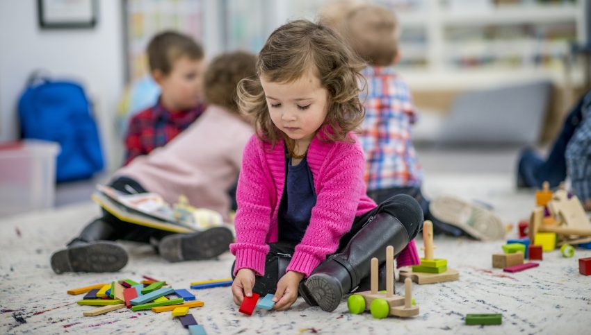 Dziewczynka w różowymswetrze siedzi na podłodze w przedszkolu i bawi się klockami
