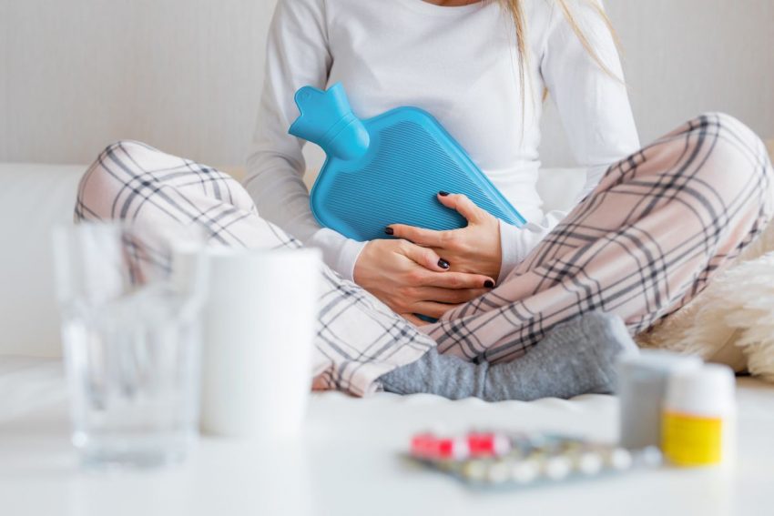 bóle menstruacyjne - kobieta z termoforem i leki