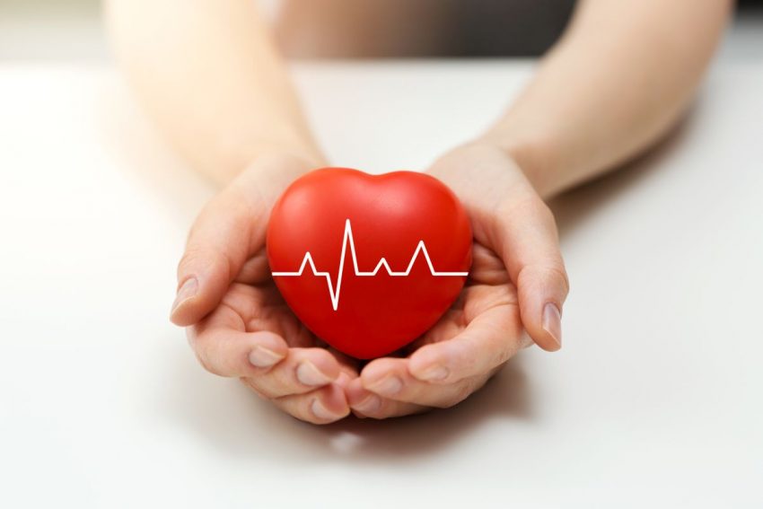 mężczyzna trzyma w dłoniach czerwone serce, na nim jest zapis ekg