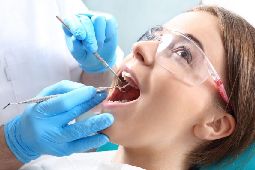 Kobieta siedzi na fotelu dentystycznym, lekarz sprawdza jej uzębienie