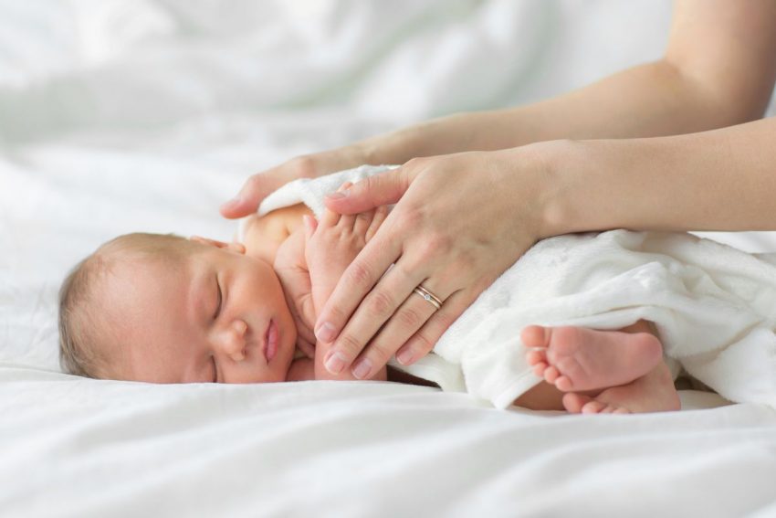 Mama dotyka dłońmi niemowlę zawinięte w pieluszkę