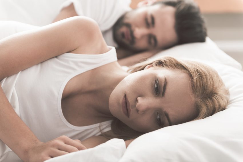 Kobieta z dyspareunią leży przygnębiona w łóżku obok swojego partnera.