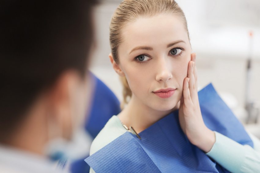 Kobieta z bólem zęba rozmawia z dentystą przed zabiegiem ekstrakcji zęba.