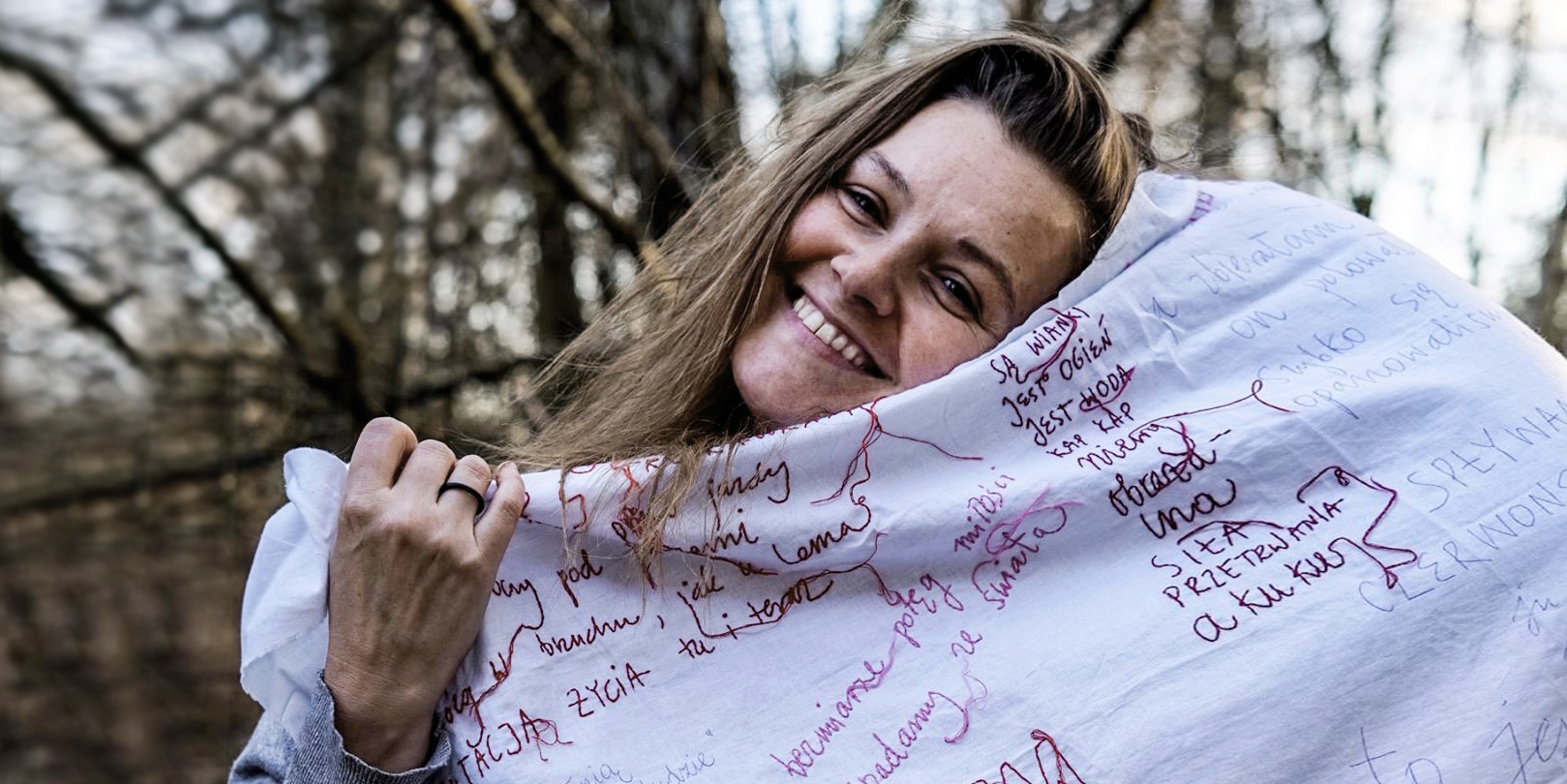 Tekst o edukacji menstruacyjnej i normalizacji okresu. Na zdjęciu: Kobieta uśmiechająca się i trzymająca koc z napisem - HelloZdrowie