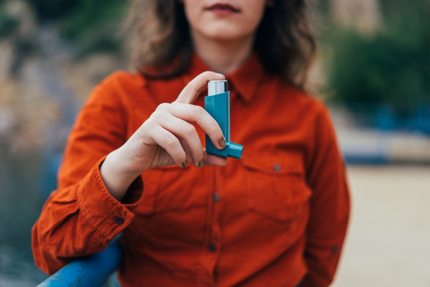 Kobieta ma astmę i trzyma w ręce inhalator, który jest na pierwszym planie.