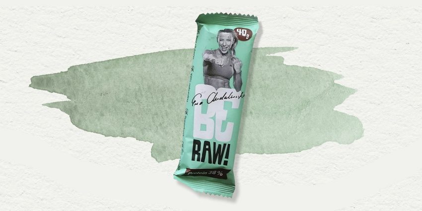 Tekst o batonach proteinowych, ich składzie i korzyściach. Na zdjęciu: Zielone opakowanie z kobietą na nim - HelloZdrowie