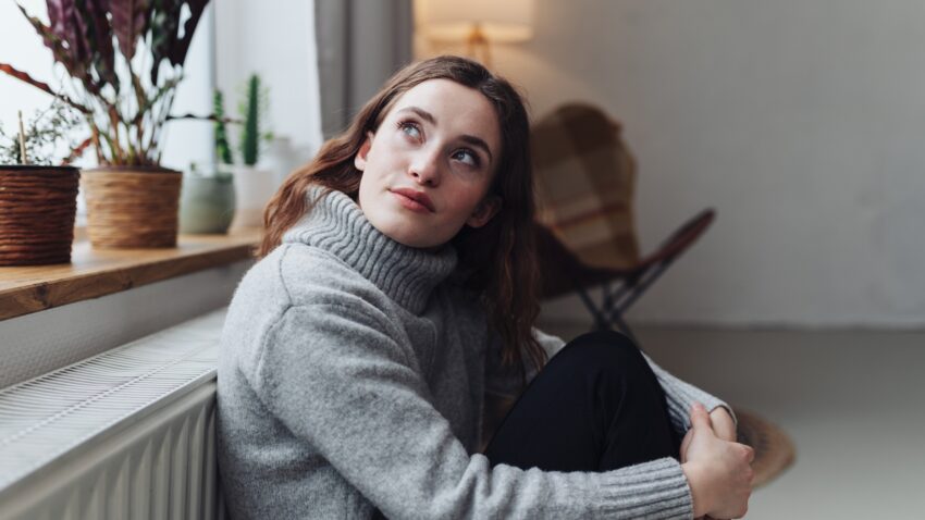 na zdjęciu: kobieta grzeje się przy kaloryferze; tekst o tym, że podkręcanie ogrzewania nie jest zdrowe - Hello Zdrowie