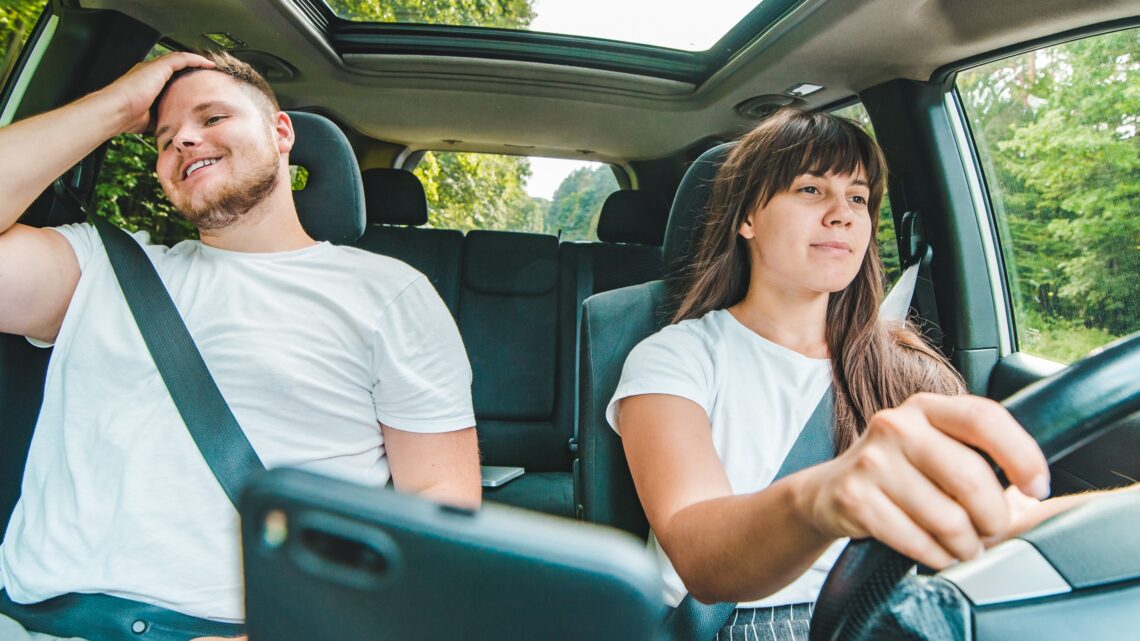 na zdjęciu: kobieta prowadzi auto, mężczyzna siedzi obok; tekst o tym, czy mężczyzna musi mieć prawo jazdy - Hello Zdrowie