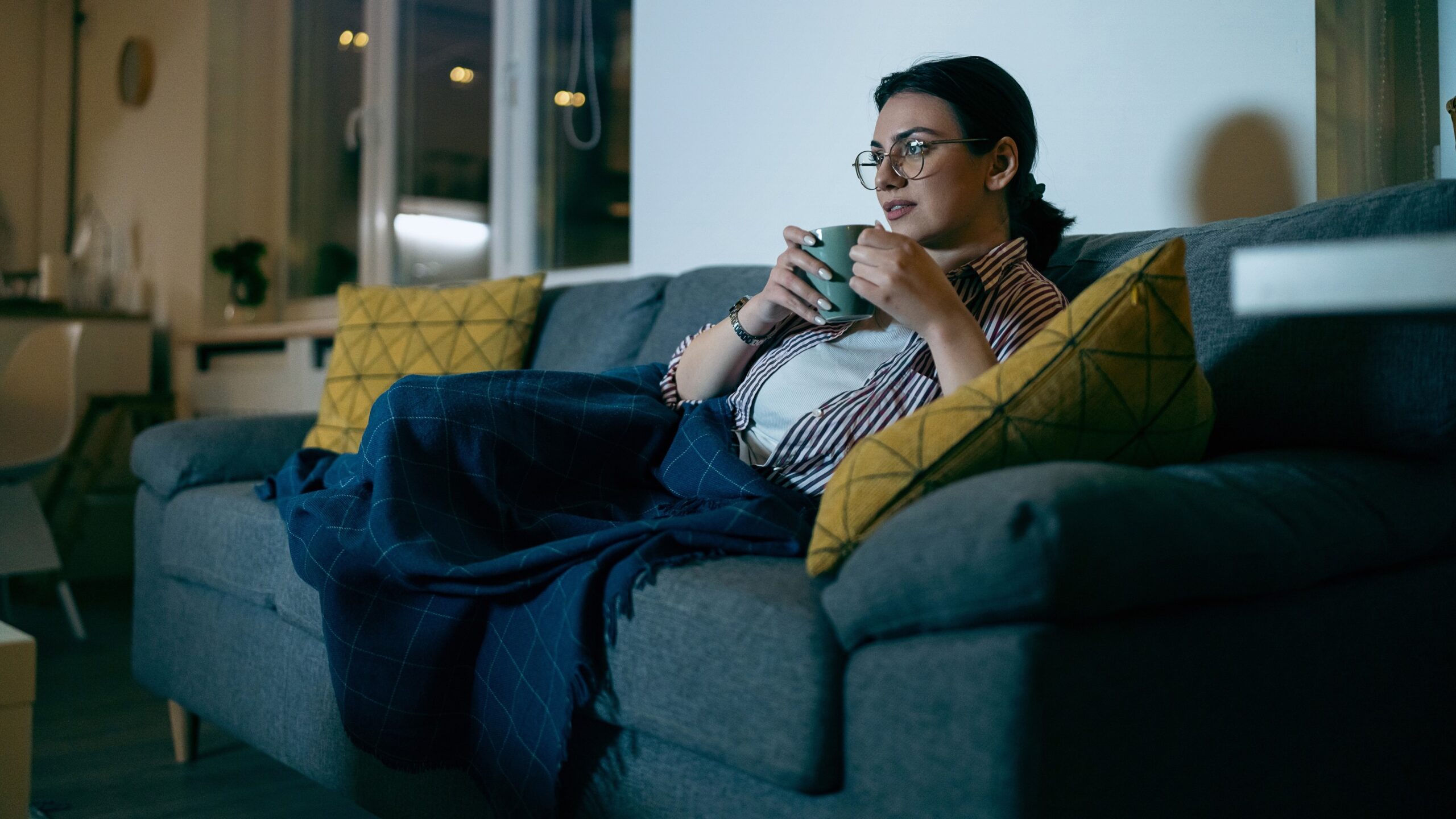 na zdjęciu: kobieta w filiżanką herbaty na kanapie ogląda telewizję, tekst o binge-watching jako nowym uzależnieniu - Hello Zdrowie