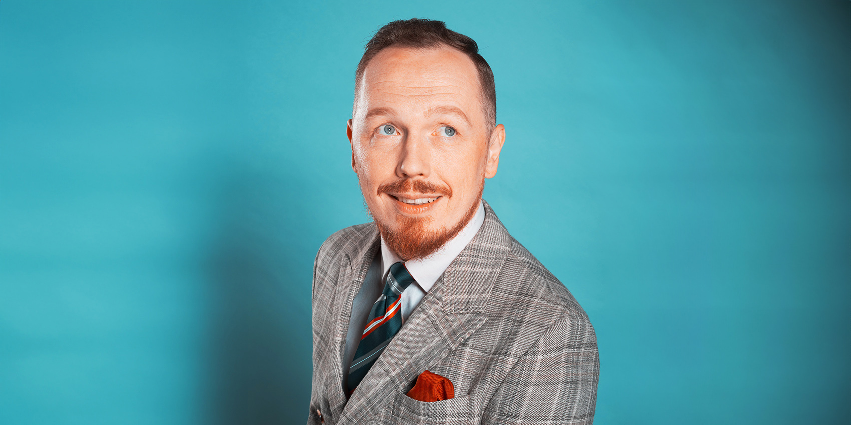 Antoni Syrek-Dąbrowski - komik w garniturze pozuje na niebieskim tle