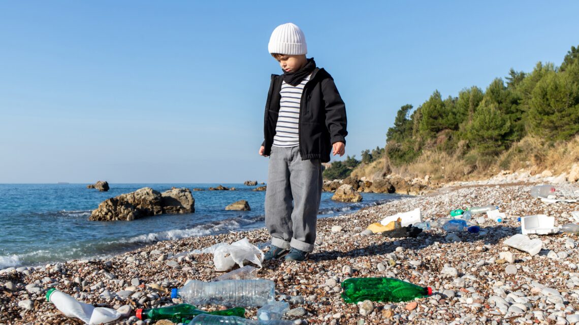 chłopiec nad brzegiem morza stoi wśród plastikowych butelek - Hello Zdrowie