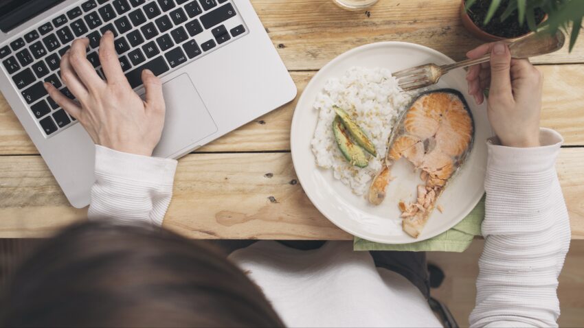 osoba pisze na laptopie, jedząc łososia z ryżem - Hello Zdrowie
