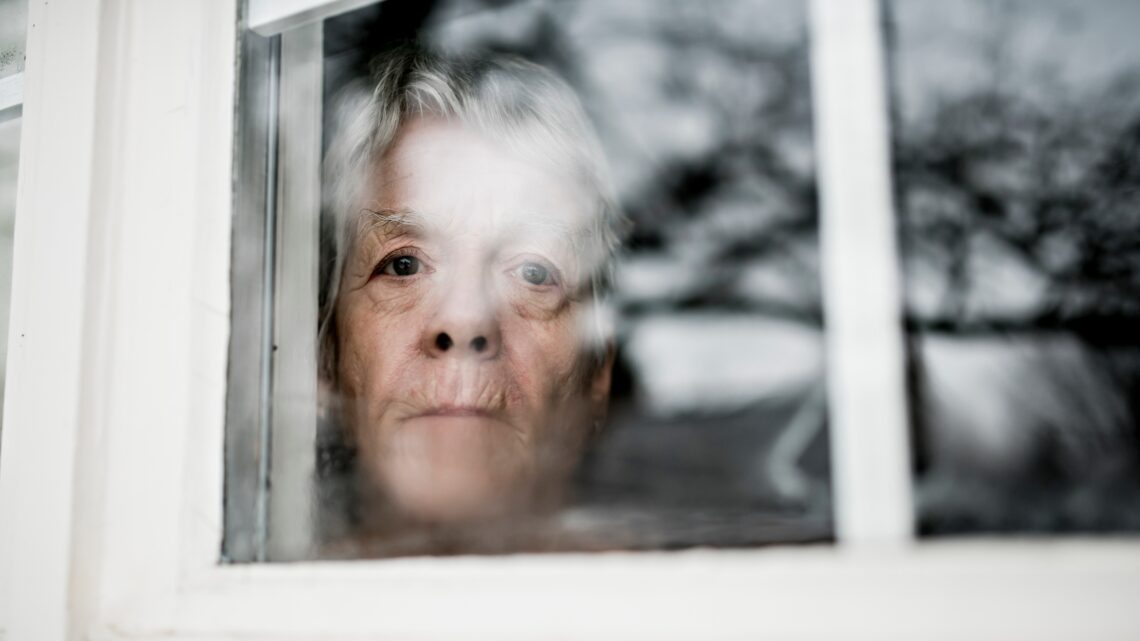 na zdjęciu: starsza kobieta patrzy przez okno, tekst o tym, że kobiety częściej chorują na alzheimera - Hello Zdrowie