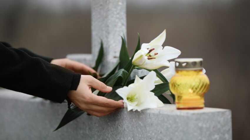 Dłoń trzymająca lilie, obok znicz