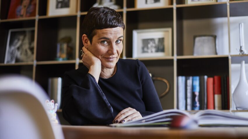 Kobieta około 50., w krótkich włosach, czyta książkę, patrząc w obiektyw aparatu - Hello Zdrowie