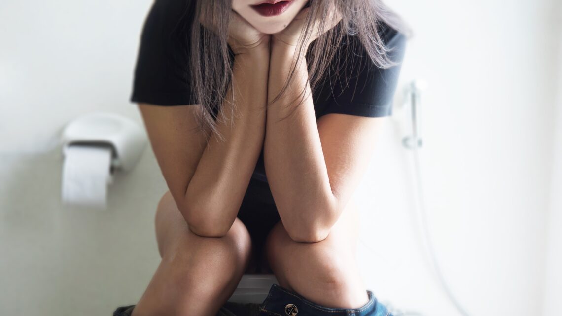 na zdjęciu: młoda kobieta siedzi na toalecie, tekst o szybkości pasażu jelitowego i jego wpływie na zdrowie - Hello Zdrowie