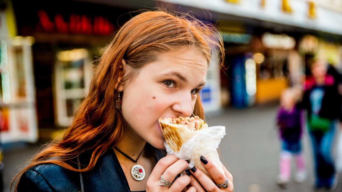 na zdjęciu: kobieta je fastfood rękami; tekst o tym, że jedzenie rękami wpływa pozytywnie na pracę jelit - Hello Zdrowie
