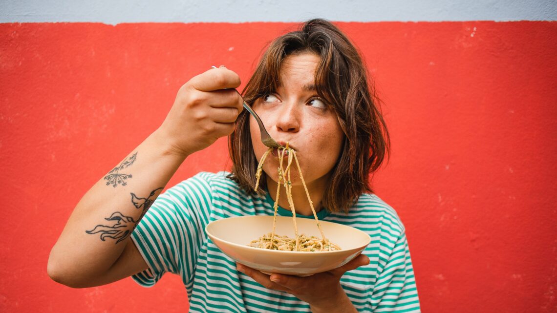 na zdjęciu: młoda kobieta je makaron; tekst o tym, jak poznać, że jelita działają prawidłowo - Hello Zdrowie