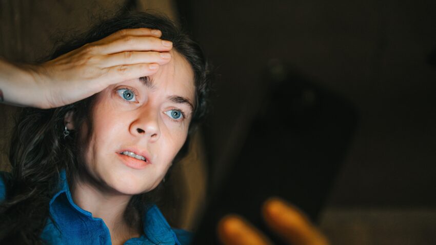 na zdjęciu: kobieta w średnim wieku ze smutkiem spogląda w telefon, tekst o mechanizmie przemocy DARVO - Hello Zdrowie