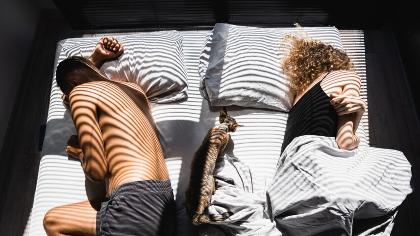 Para leży w łóżku plecami do siebie, pada na nich światło przez żaluzje - Hello Zdrowie