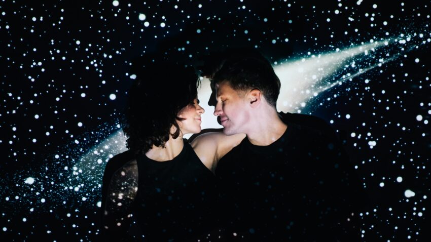 ubrana na czarno para przytula się na tle wyświetlanej na ścianie Drogi Mlecznej - Hello Zdrowie