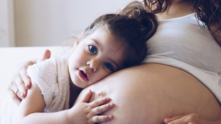 Dziewczynka obejmuje brzuch mamy w ciąży - Hello Zdrowie