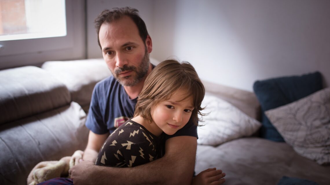 na zdjęciu: ojciec z synem na kolanach siedzi na kanapie, tekst o rodzicach, którzy nie chcą się pogodzić z diagnozą autyzmu u swoich dzieci - Hello Zdrowie