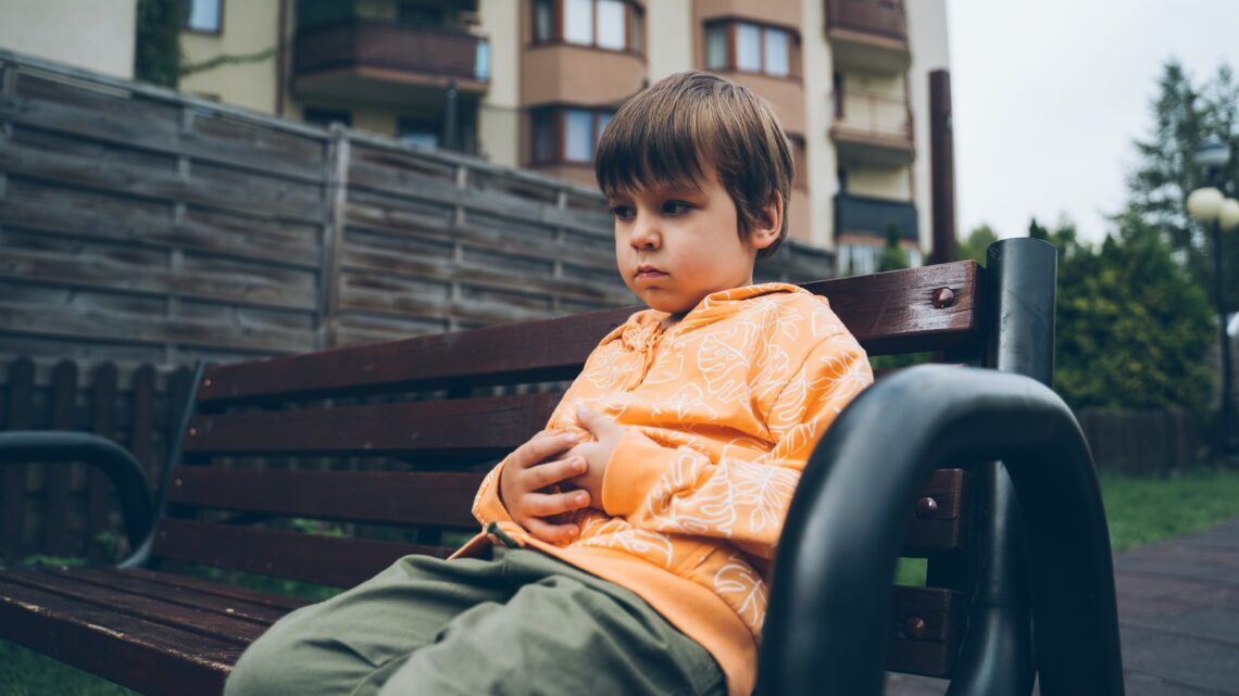 chłopiec siedzi na ławce przed blokiem, trzyma się za brzuszek - Hello Zdrowie