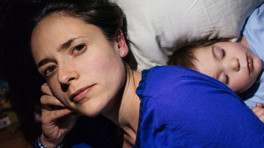 Kobieta leżąca ze śpiącym dzieckiem na łóżku - Hello Zdrowie