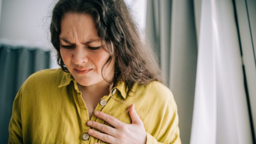 na zdjęciu: kobieta trzyma się za klatkę piersiową i marszczy czoło; tekst o tym, że wyniki w normie nie zawsze są ok - Hello Zdrowie