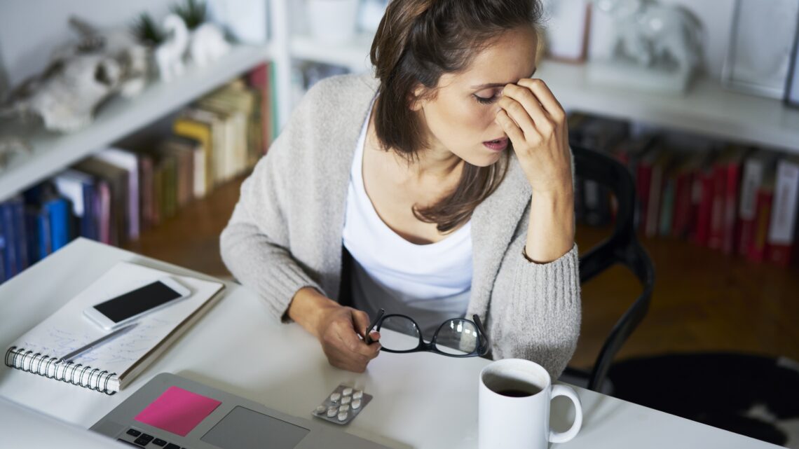zmęczona kobieta pociera czoło, przed nią leży blister tabletek - Hello Zdrowie
