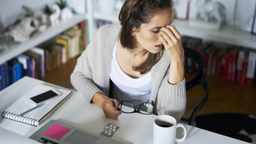 zmęczona kobieta pociera czoło, przed nią leży blister tabletek - Hello Zdrowie